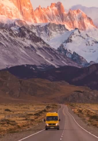 Keltainen matkailuauto avoimella tiellä lumihuippuisen Fitz Roy -vuoren alla Patagoniassa